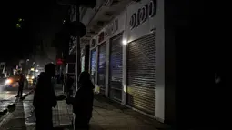 Kebijakan ini direncanakan berlaku selama satu bulan sebelum dievaluasi kembali. Tampak dalam foto, orang-orang berdiri di dekat toko-toko yang tutup lebih awal karena jam malam yang diberlakukan pemerintah untuk mengurangi biaya energi di pusat kota Kairo, Mesir, pada Kamis 2 April 2026. (Khaled DESOUKI/AFP)