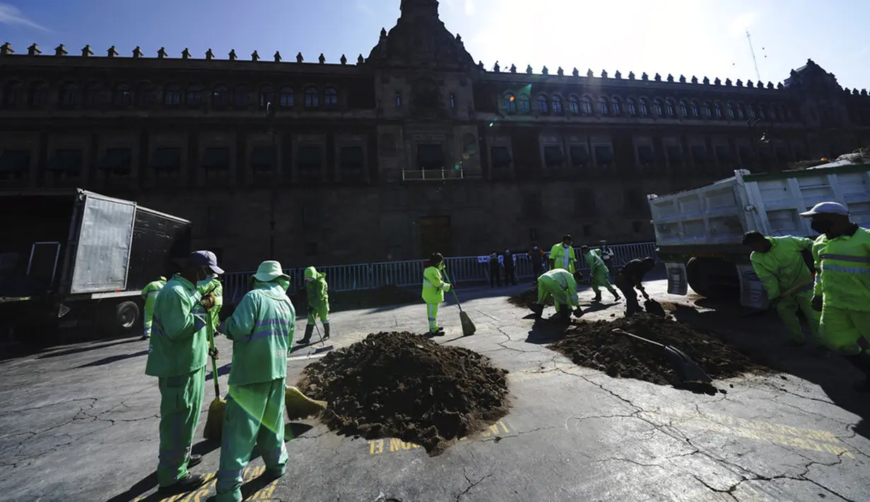 Pekerja kota membersihkan tumpukan tanah yang melambangkan kuburan klandestin buatan orang-orang yang kehilangan anggota keluarga saat menuntut jawaban dari pemerintah di luar Istana Nasional, Mexico City, Meksiko, 13 Desember 2021. (AP Photo/Marco Ugarte)