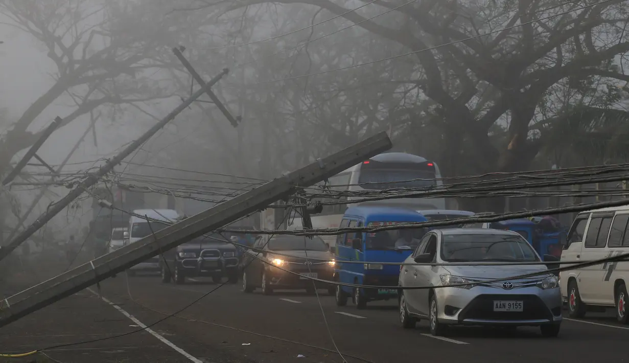 Sejumlah kendaraan melewati tiang listrik yang roboh akibat angin kencang yang disebabkan Topan Nock-ten di kota Pili, Camarines sur, Filipina tengah (27/12). Topan Nock-ten atau dikenal dengan Nina menerjang Filipina saat Natal. (REUTERS/Romeo Ranoco)