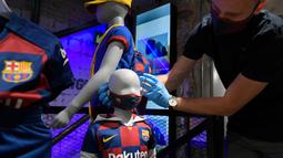 Penjaga toko memasang masker berlogo Barcelona ke Manekin di Toko Asesoris Barcelona, Senin (25/5/2020). Di tengah pandemi virus Corona, Barcelona menjual masker dengan harga 18 euro atau sekitar Rp 291 ribu. (AFP/Lluis Gene)