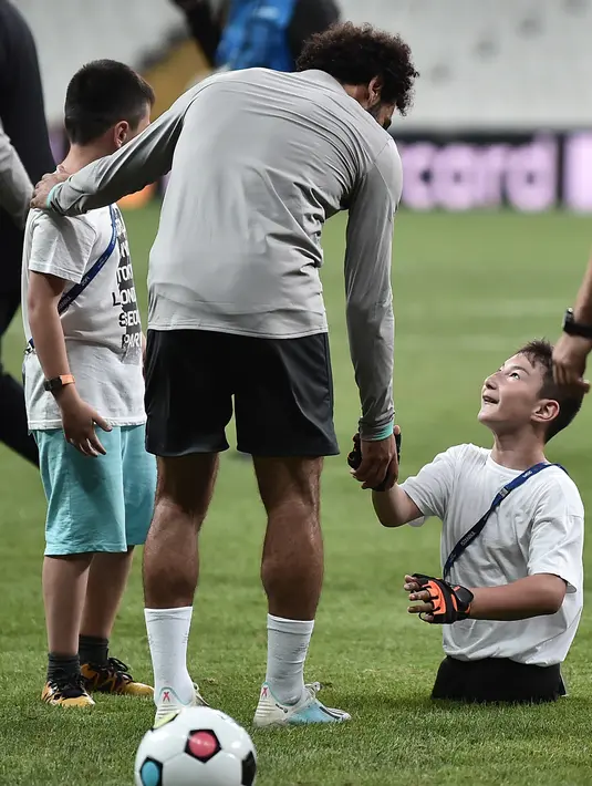 Seorang anak tanpa memiliki kaki bersalaman dengan Gelandang Liverpool, Mohamed Salah saat sesi pelatihan jelang bertanding melawan Chelsea pada Piala Super Eropa 2019 di Stadion Taman Besiktas, di Istanbul (13/8/2019). (AFP Photo/Ozan Kose)