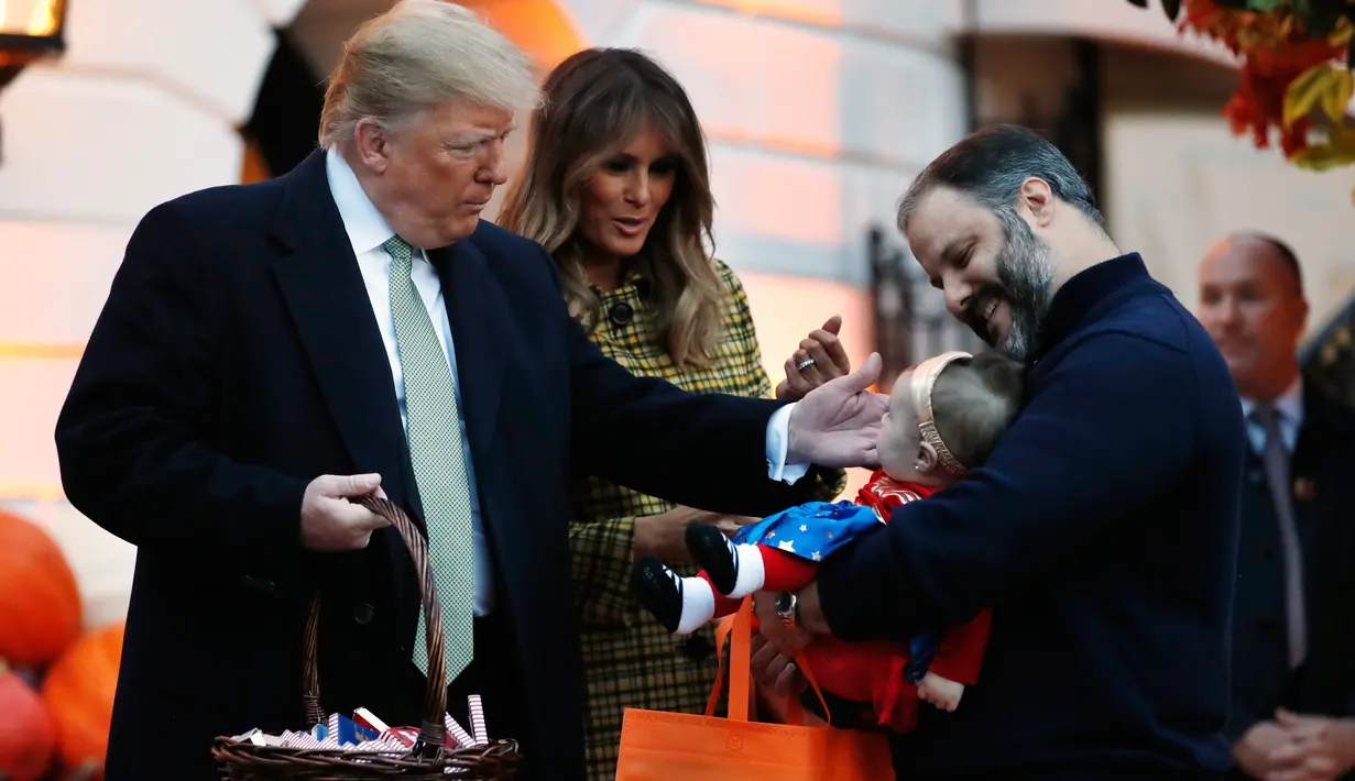 Presiden AS Donald Trump dan Melania Trump menyapa seorang bayi berkostum superhero saat mereka membagikan permen kepada anak-anak selama acara trick-or-treat pada perayaan Halloween di Gedung Putih, Washington, Minggu (28/10). (AP/Jacquelyn Martin)