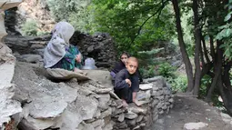 Anak-anak duduk di atas bebatuan setelah banjir bandang menghantam wilayah Ursoon, daerah terpencil Chitral di Pakistan utara, Minggu (3/7). Banjir bandang akibat hujan lebat yang lama itu telah menewaskan sedikitnya 43 orang. (GUL HAMAAD Farooqi/AFP)