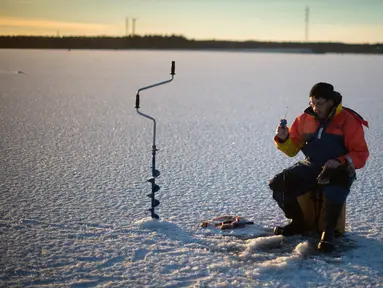 Seorang pria berusaha memancing ikan di laut Bothnia yang sedang membeku, Vaasa, Finlandia (29/12). Kebiasaan memancing di laut beku merupakan hal menantang yang ditunggu-tunggu oleh sebagian warga setempat. (AFP PHOTO/Olivier Morin)