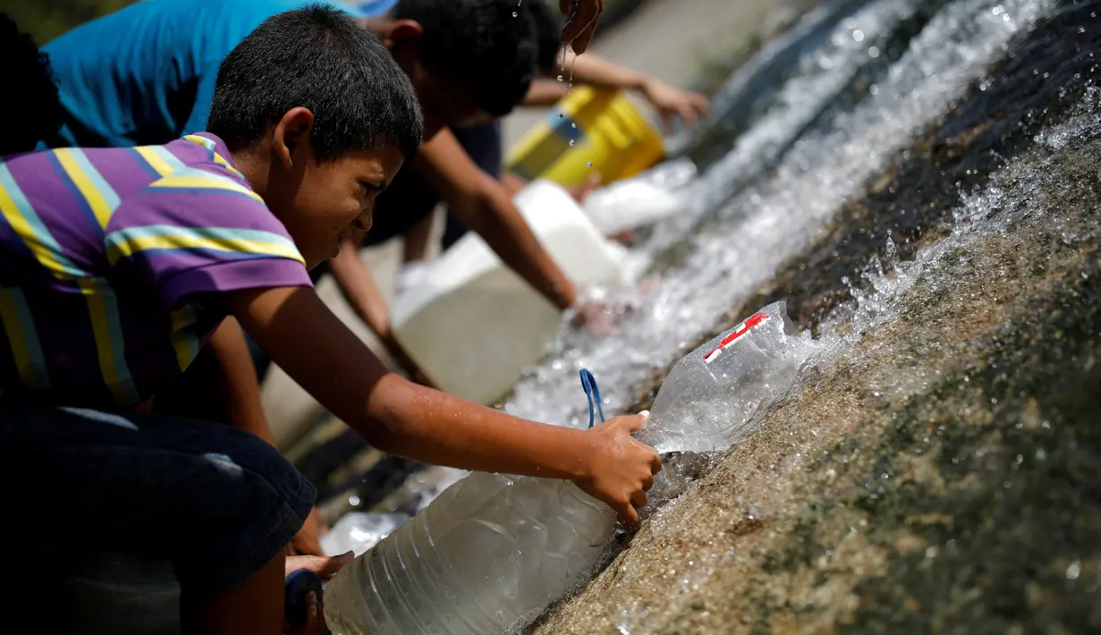 Seorang anak mengumpulkan air yang keluar melalui saluran pembuangan air limbah yang mengalir ke Sungai Guaire di Caracas, 11 Maret 2019.  Pemadaman listrik selama berhari-hari di Venezuela berdampak terhadap krisis air. (REUTERS/Carlos Garcia Rawlins)