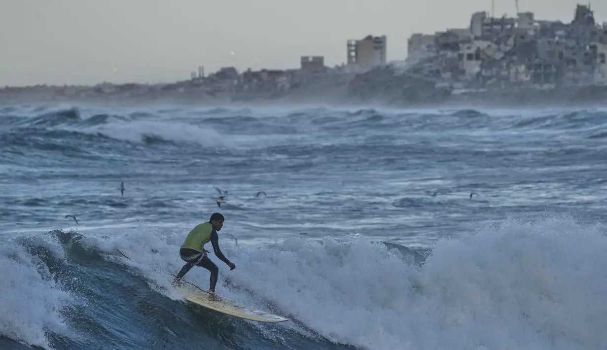 Meski, sepanjang garis pantai menunjukkan kerusakan nyata dengan puing-puing bangunan di sekitarnya. Tampak dalam foto, Khalil Abu Jayyab, warga Palestina, berselancar di pantai Kota Gaza, Minggu, 28 Desember 2025. (AP Photo/Jehad Alshrafi)