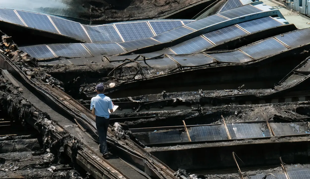 Seorang penyidik berjalan di tengah panel surya yang terbakar di sebuah taman air Taipei, Taiwan, (28/7). Menurut otoritas setempat, korsleting dipicu oleh gelombang panas yang membuat suhu di Taipei mencapai 38,5 derajat celcius. (AFP PHOTO/SAM YEH)