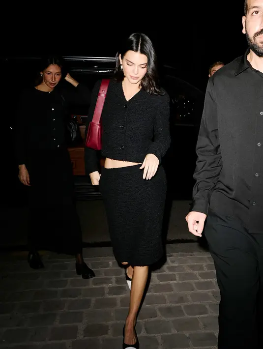 Kendall Jenner tampil minimalis dengan cardigan dan rok mini hitam. Ia jinjing tas Chanel merah dan flatshoes dual tone [Chanel]