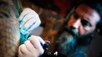 Seorang seniman mentato badan pengunjung dalam acara edisi keempat Montreux Tattoo Convention di Montreux, Swiss  (22/9). Montreux Tattoo Convention berlangsung selama tiga hari. (Valentin Flauraud/Keystone via AP)