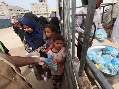 Seorang anak pengungsi Palestina mengambil sebungkus roti sementara yang lain menunggu giliran mereka dari salah satu dapur amal di kamp pengungsi Bureij, Jalur Gaza Tengah pada Senin 18 Mei 2026. (Eyad Baba/AFP)