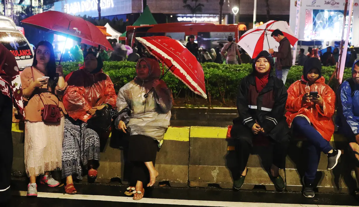 Masyarakat beristirahat saat car free night di kawasan Thamrin, Jakarta, Selasa (31/12/2019). Meski diguyur hujan masyarakat mulai memadati kawasan tersebut untuk menikmati malam pergantian tahun 2019. (Liputan6.com/Angga Yuniar)