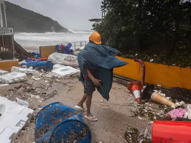 Seorang pria berjalan melewati puing-puing yang tersisa di pantai saat Topan Super Ragasa melintas di Hong Kong pada 24 September 2025. (Dale DE LA REY/AFP)