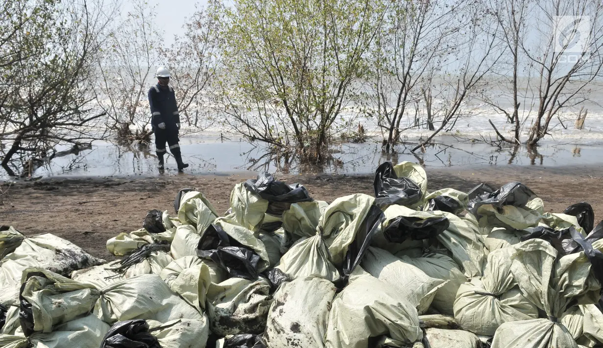 Pegawai Pertamina melintas di depan tumpukkan karung berisi limbah tumpahan minyak (oil spill) di Pantai Muara Beting, Muara Gembong, Bekasi, Jawa Barat, Minggu (28/7/2019). Oil spill akibat kebocoran terjadi di sumur lepas pantai YYA1 Karawang. (merdeka.com/Iqbal S. Nugroho)