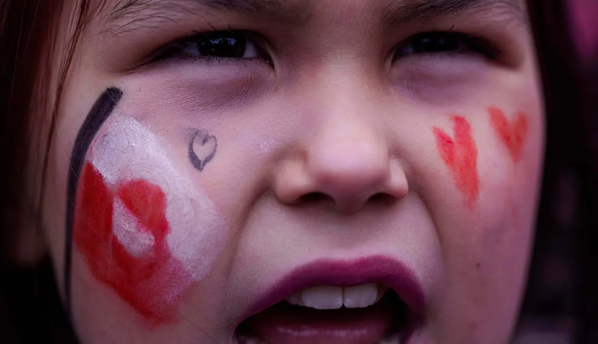 Bendera merah-putih Greenland berkibar di antara sejumlah poster penolakan. Tampak dalam foto, seorang gadis berteriak saat protes menentang kebijakan Presiden Amerika Serikat (AS), Donald Trump, terhadap Greenland di depan konsulat AS di Nuuk, Sabtu 17 Januari 2026. (AP Photo/Evgeniy Maloletka)