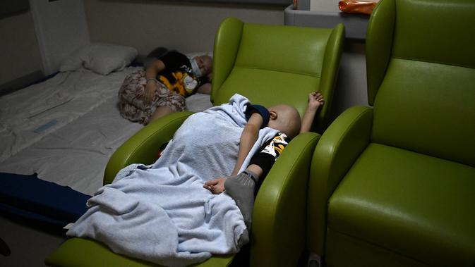 Anak-anak yang berjuang melawan kanker dipindahkan ke ruang bawah tanah pusat onkologi yang digunakan sebagai tempat perlindungan bom, di Kiev, Senin (28/2/2022). Tentara Rusia mengatakan, warga sipil Ukraina dapat meninggalkan ibu kota Kiev dengan bebas. (Aris Messinis / AFP)
