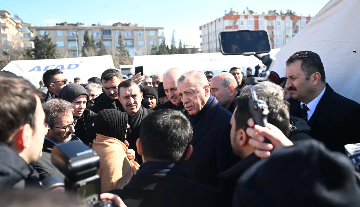 Presiden Turki Recep Tayyip Erdogan bertemu dengan penduduk yang mengungsi di bawah tenda yang didirikan pemerintah selama kunjungannya ke kota Kahramanmaras di tenggara Turki, dua hari setelah gempa kuat melanda wilayah tersebut, pada 8 Februari 2023. Di tengah hujan dingin dan salju warga mengungsi salju di masjid, sekolah dan bahkan halte bus. (AFP/Ozan Kose)
