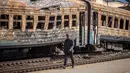Seorang pria berjalan di depan kereta api yang hancur di timur laut kota Trostianets (29/3/2022). Ukraina mengatakan pasukannya telah merebut kembali kota Trostianets, dekat perbatasan Rusia, salah satu kota pertama yang jatuh di bawah Kontrol Moskow dalam invasi selama sebulan. (AFP/Fadel Senna)