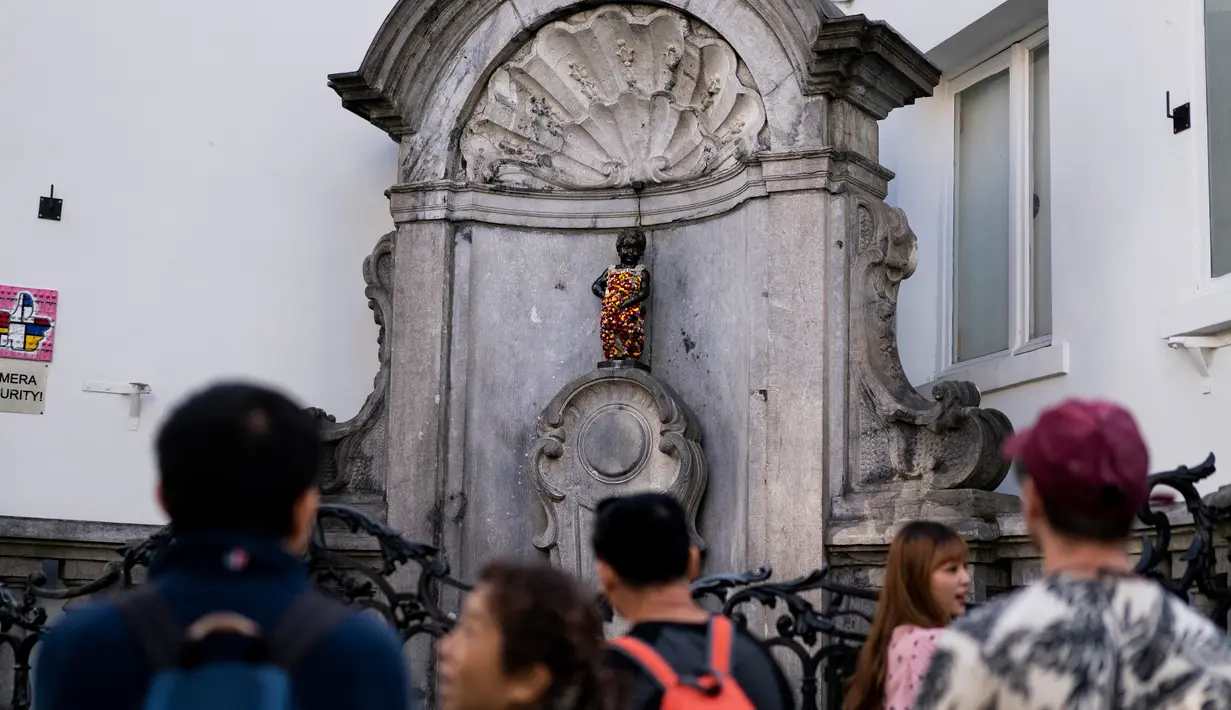 Wisatawan berfoto dekat patung 'Manneken Pis' dalam balutan baju bermotif bunga di ibu kota Belgia, Brussels, Senin (12/8/2019). Patung anak laki-laki yang sedang buang air kecil ini menjadi salah satu daya tarik uta di kota cantik tersebut. (Photo by Kenzo TRIBOUILLARD / AFP)