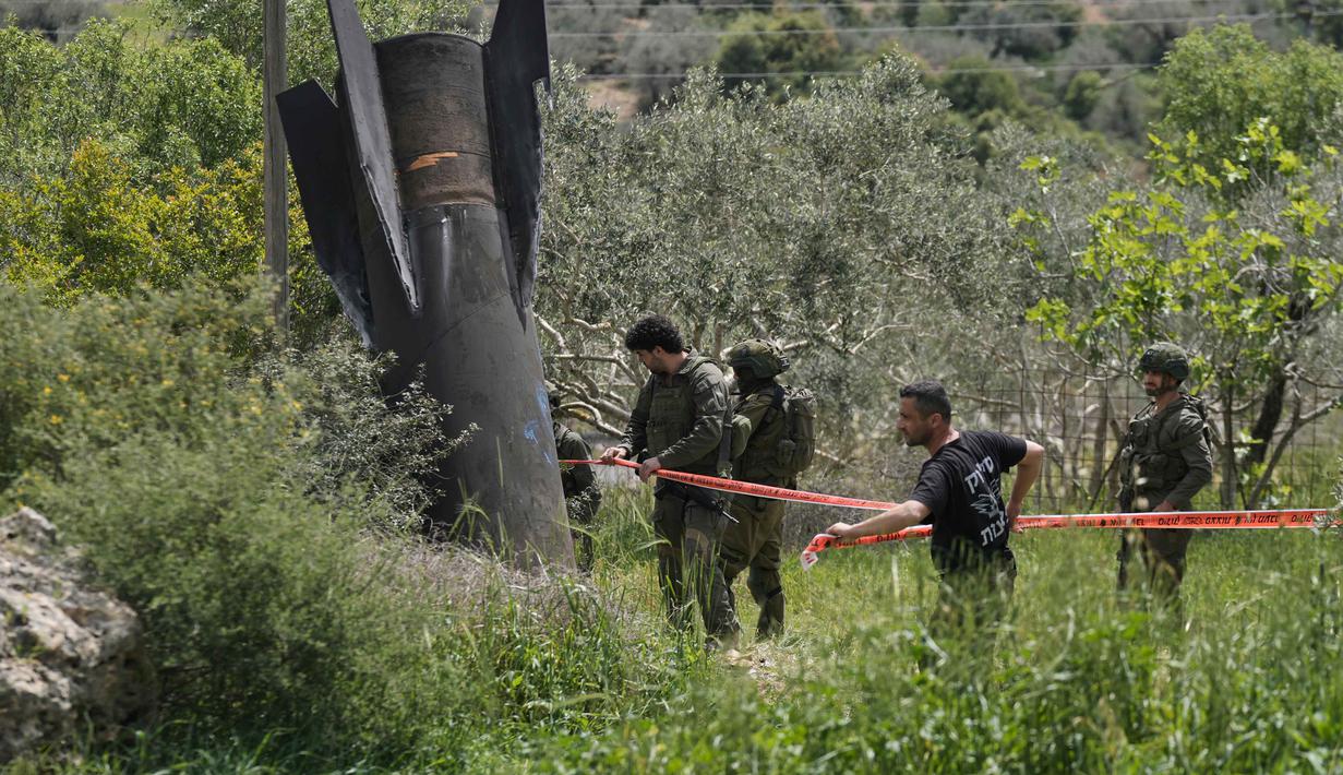 Potongan besar rudal tersebut jatuh di area terbuka dan menjadi pusat perhatian warga setempat yang berdatangan untuk melihat langsung. Tampak dalam foto, personel militer Israel mengamankan lokasi jatuhnya puing-puing rudal Iran di desa Kifl Haris, Tepi Barat, Selasa, 24 Maret 2026. (AP Photo/Majdi Mohammed)