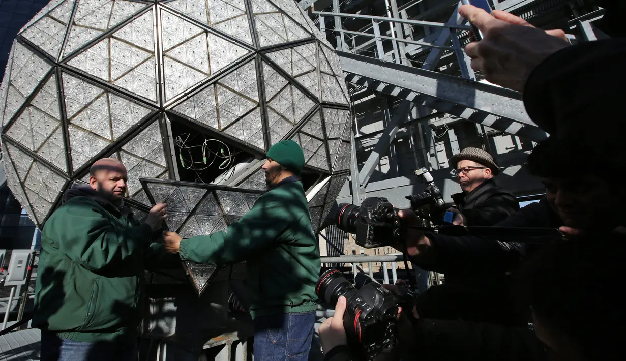 Awak media melihat pekerja menyelesaikan pemasangan bola kristal di atas sebuah gedung di Times Square, New York, Kamis (27/12). Menyaksikan bola kristal raksasa adalah tradisi yang tidak terlewatkan setiap perayaan tahun baru sejak 1907. (AP/Seth Wenig)