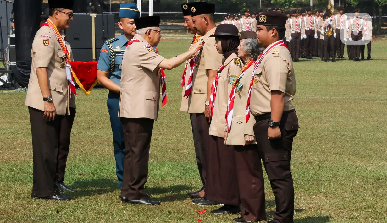 Wakil Presiden Ma`ruf Amin (tengah) didampingi Ketua Kwartir Nasional (Kwarnas) Pramuka Budi Waseso (kiri) menyematkan tanda penghargaan kepada anggota Pramuka di Bumi Perkemahan dan Graha Wisata (Buperta) Cibubur, Jakarta, Rabu (14/8/2024). (Liputan6.com/Herman Zakharia)