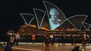 Orang-orang menyaksikan Sydney Opera House diterangi untuk menghormati Ratu Elizabeth II di Sydney, Australia, Jumat (9/9/2022). Sejumlah tempat pun turut menyampaikan duka cita atas meninggalnya sang ratu dengan berbagai cara, mulai dari mematikan lampu pencahayaan hingga mengibarkan bendera setengah tiang. (AP Photo/Mark Baker)