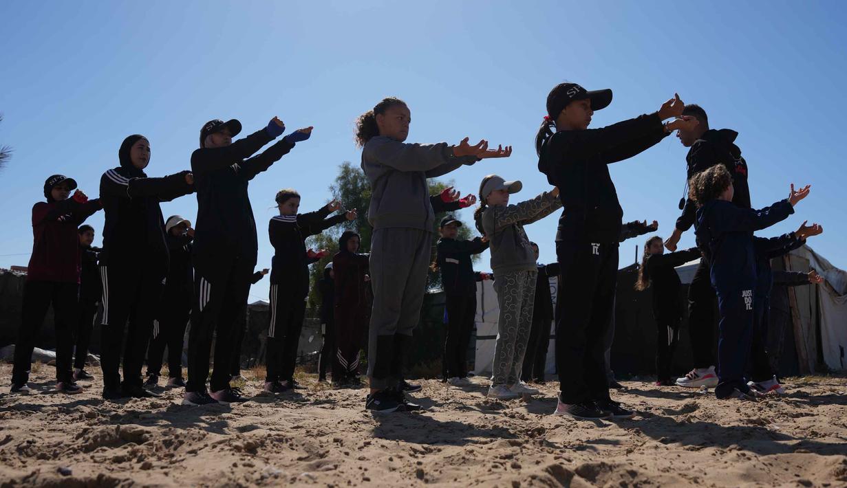 Mereka berlatih tinju, bukan untuk berkompetisi, melainkan sebagai terapi psikologis dan cara untuk bertahan hidup di tengah tekanan perang yang berkepanjangan. Tampak dalam foto, gadis-gadis Palestina melakukan pemanasan sebelum latihan di klub tinju wanita di Khan Younis, Jalur Gaza Selatan, Rabu 6 Mei 2026. (AP Photo/Abdel Kareem Hana)