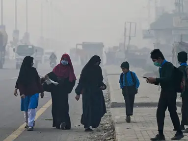 Para siswa mengenakan masker saat mereka berjalan ke sekolah di tengah kabut asap pekat di Lahore, Pakistan pada 24 November 2023. (Arif ALI/AFP)