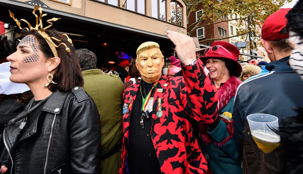 Seorang pria dengan topeng Donald Trump bersuka cita saat puluhan ribu orang menyambut dimulainya musim karnaval di jalan-jalan Kota Cologne, Jerman, Senin (11/11/2019). Tradisi ini akan dimulai tepat pada jam 11.11, tanggal 11, dan bulan sebelas. (AP Photo/Martin Meissner)