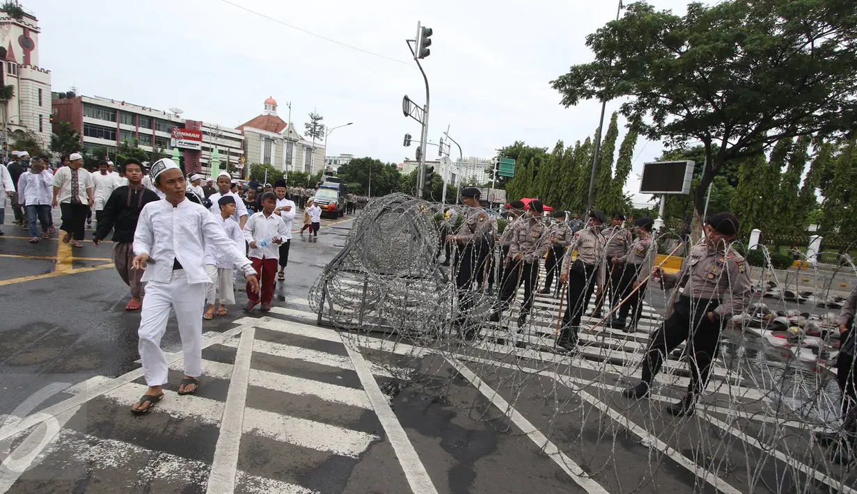 Massa aksi 31 Maret melintasi petugas polisi yang sedang memasang kawat berduri di sekitar Istana Negara, Jakarta, Jumat (31/3). Kawat berduri tersebut dipasang untuk mengantisipasi ricuh aksi 31 Maret. (Liputan6.com/Immanuel Antonius)