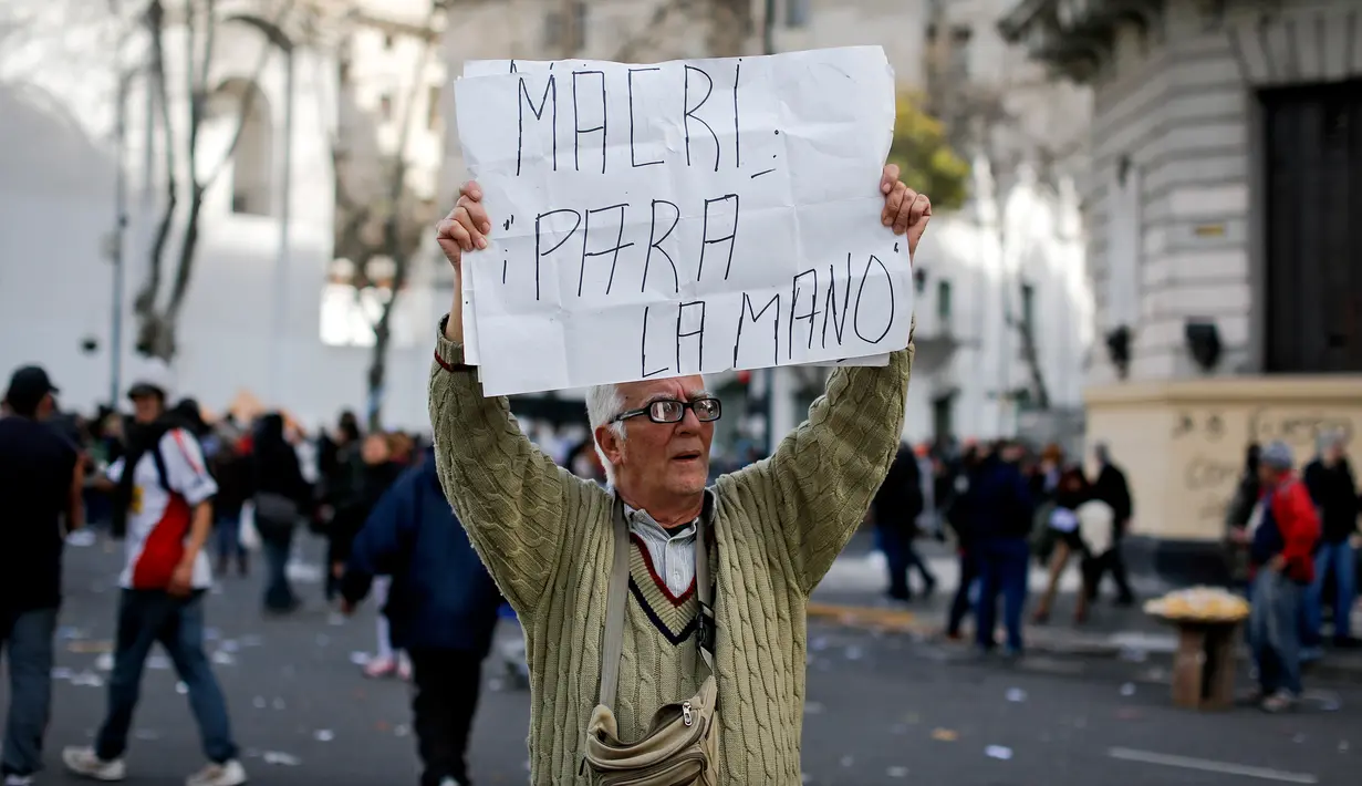 Pria paruh baya membawa papan berisi “Macri, hentikan!” dalam bahasa Spanyol saat demonstrasi di Plaza de Mayo, Buenos Aires, Argentina, Selasa (22/8). Macri berusaha menurunkan upah para buruh demi menghasilkan Investasi lebih. (Victor R. Caivano/AP)