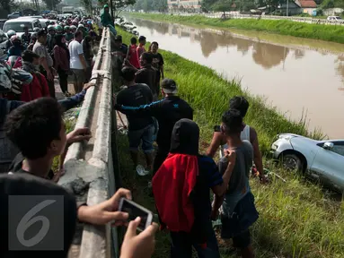 Warga menyaksikan proses evakuasi mobil yang terperosok di saluran Ispeksi Kalimalang, Jabar, Minggu (7/5). Minibus bernopol B 1475 FRK itu tercebur kedalam saluran inspeksi Kalimalang dan sempat terseret arus sejauh 100m. (Liputan6.com/Gempur M Surya)