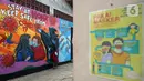 Seorang anak berdiri depan mural bertema virus corona COVID-19 yang menghiasi dinding rumah di kawasan Pangkalan Jati Baru, Depok, Jawa Barat, Selasa (2/6/2020). Mural bertulis ‘Stay At Home, Keep Safe From COVID-19’ itu untuk mengingatkan warga akan bahaya COVID-19. (Liputan6.com/Johan Tallo)