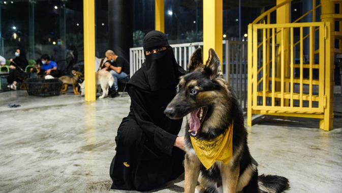 Seorang perempuan duduk dengan anjing herdernya di kafe 