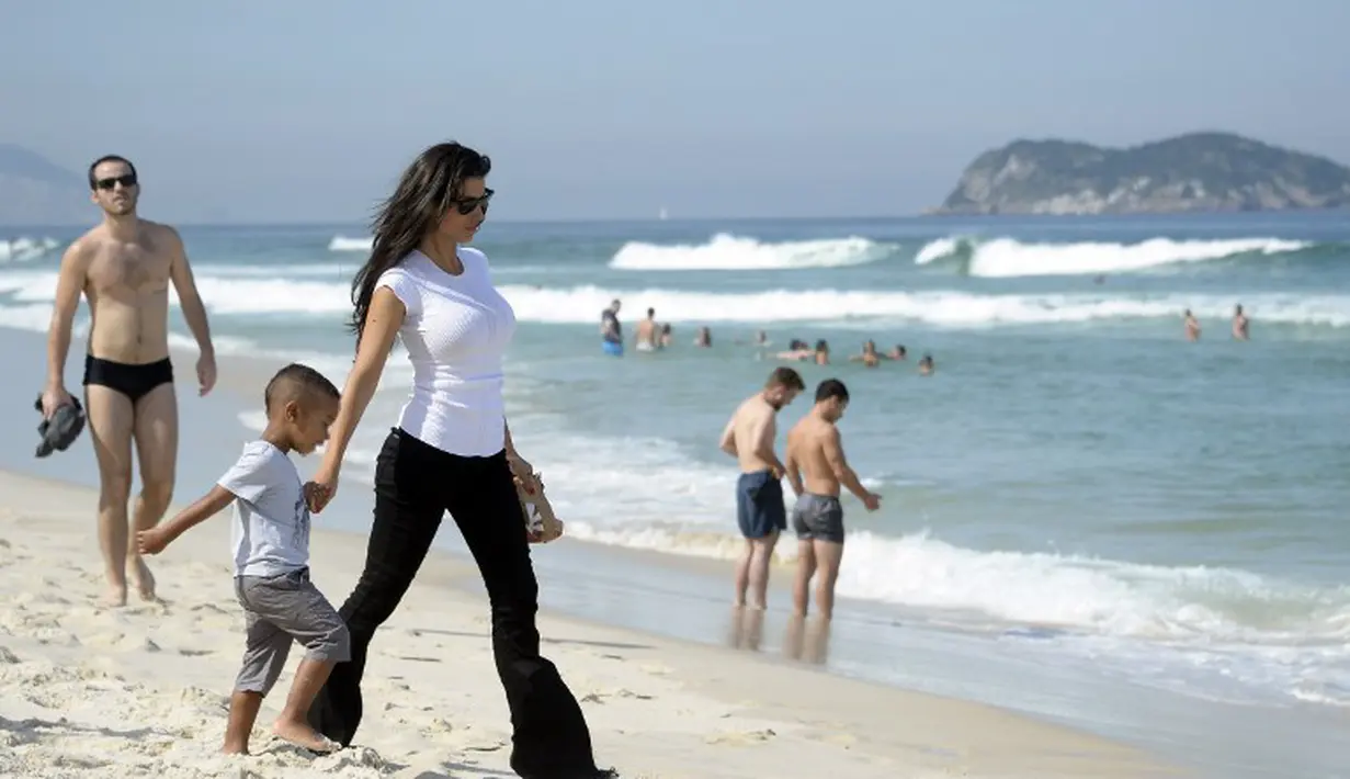 Ludivine Kadri memegang tangan buah hatinya saat berkunjung di Pantai Rio de Janeiro, Brasil (26/6/2014) (AFP PHOTO/FRANCK FIFE)
