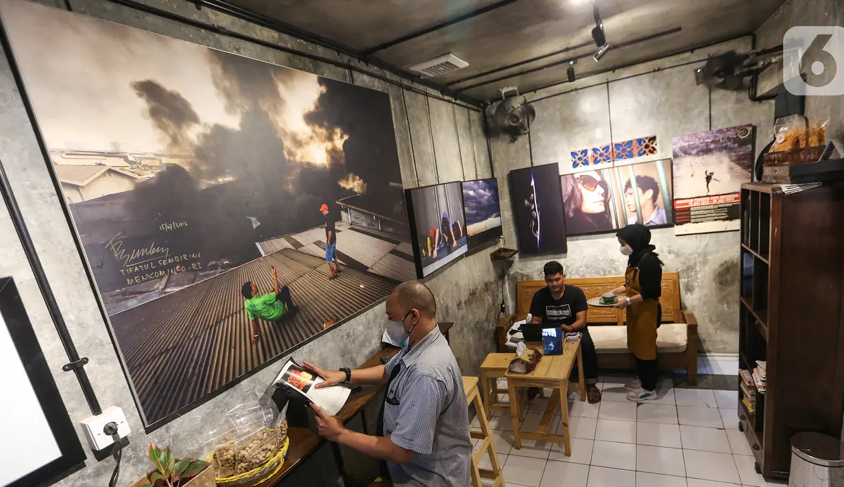 Pengunjung melihat buku fotografi sambil menikmati kopi di kedai Ngopi di Halaman Jalan Pulo Kamboja, Kebayoran Lama, Jakarta, Selasa (12/01/2021). Kedai yang menawarkan beragam jenis minuman kopi dan makanan ringan memajang puluhan karya foto para Pewarta Foto Indonesia. (Liputan6.com/Fery Pradolo)