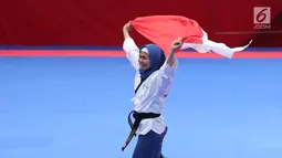 Atlet Taekwondo putri Indonesia, Defia Rosmaniar mengibarkan bendera Merah Putih saat merayakan kemenangan atas Salahshouri Marjan (Iran) pada Final Women Individual Poomsae di JCC, Jakarta, Minggu (19/8). (Liputan6.com/Helmi Fithriansyah)