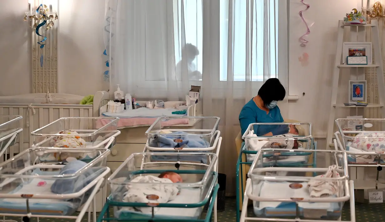 Perawat merawat bayi yang baru lahir dari skema ibu pengganti (surrogate mother) di Hotel Venice, Kiev, Ukraina, 15 Mei 2020. Hingga kini, 100 bayi itu masih menanti orangtua mereka yang berasal dari 12 negara termasuk Inggris, AS, Italia, China, Meksiko, Jerman, dan Prancis. (Sergei SUPINSKY/AFP)