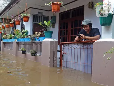 Warga bermain ponsel saat banjir merendam RW 06 kawasan Mekarsari, Depok, Jawa Barat, Sabtu (20/2/2021). Banjir yang disebabkan meluapnya aliran Kali Cipinang Timur ini terjadi akibat intensitas hujan tinggi di wilayah tersebut (Liputan6.com/Herman Zakharia)