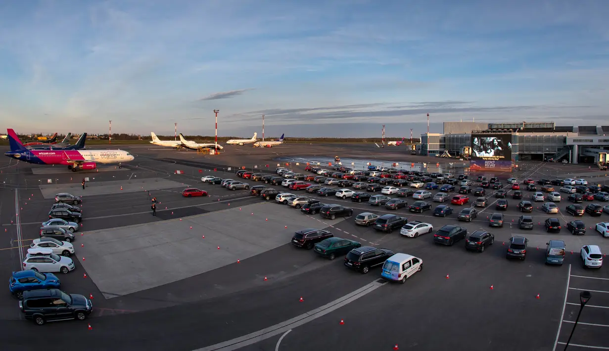 Orang-orang duduk di mobil mereka saat menonton film di bioskop drive-in di area apron bandara kota Vilnius, Lithuania pada 29 April 2020. Bandara tersebut kini sepi penumpang, akibat pembatasan perjalanan internasional untuk mengatasi penyebaran virus corona covid-19. (AP/Mindaugas Kulbis)