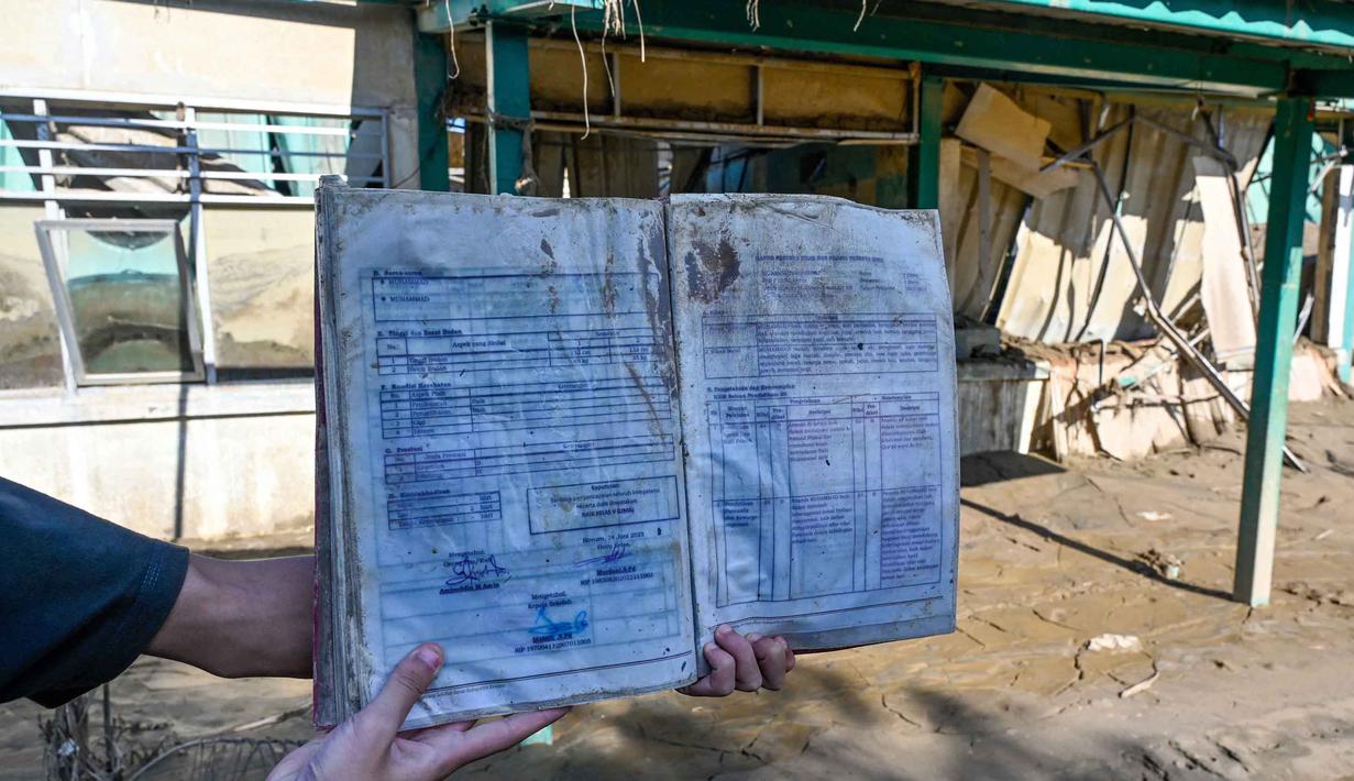 Untuk diketahui, secara resmi, Dinas Pendidikan dan Kebudayaan (Disdikbud) Bireuen telah menetapkan jadwal masuk sekolah usai libur semester pada Senin (5/1/2025). Tampak dalam foto, seseorang membawa buku laporan siswa di sebuah sekolah dasar yang hancur akibat banjir bandang di daerah yang berdekatan dengan Sungai Peusangan di Bireuen, provinsi Aceh, Senin 5 Januari 2026. (CHAIDEER MAHYUDDIN/AFP)
