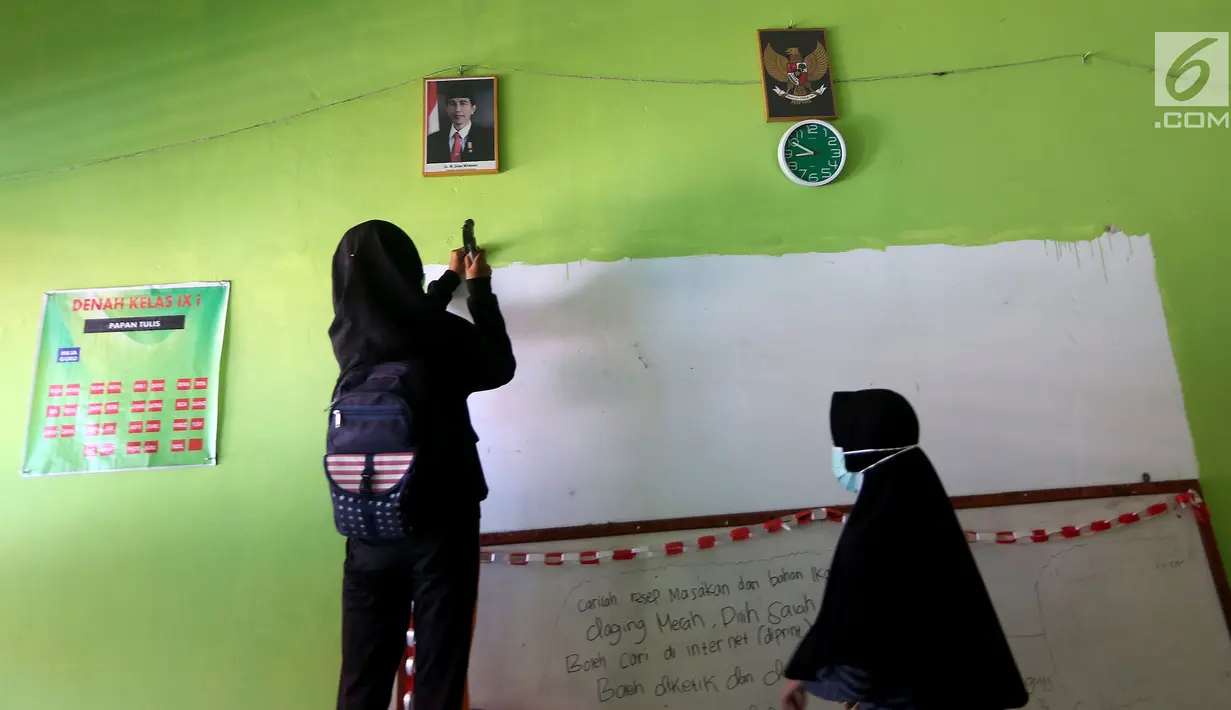Sejumlah siswi memasang papan tulis yang jatuh akibat gempa di dalam kelas SMP Negeri 6 Palu, Sulawesi Tengah, Senin (8/10). Pascagempa dan tsunami Palu, pihak sekolah melakukan pendataan untuk mengetahui jumlah siswa sekolah. (Liputan6.com/Fery Pradolo)