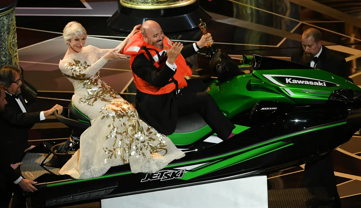 Mark Bridges mengenakan pelampung sambil memegang piala duduk di atas jet ski dalam acara Academy Awards ke-90 di Hollywood, California (4/3). Mark Bridges juga membawa pulang hadiah jet ski karena pidato terpendeknya. (Kevin Winter / Getty Images / AFP)