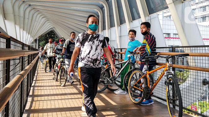 Warga melewati jembatan penyeberangan orang saat berolahraga menggunakan sepeda di sepanjang Jalan Sudirman, Jakarta, Minggu (26/7/2020). Perluasan jalur sepeda sementara dilakukan sebagai dampak peniadaan hari bebas kendaraan bermotor (HBKB) di Jalan Sudirman-Thamrin. (Liputan6.com/Faizal Fanani)