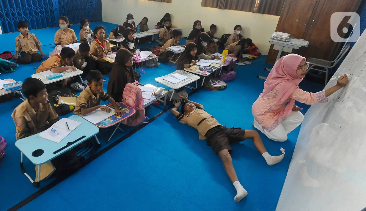 Seorang guru mengajar murid tanpa menggunakan meja dan kursi sekolah, di SDN Bojong Nangka 02, Kabupaten Bogor, Jawa Barat, Kamis (16/2/2023). Sudah lebih dari dua pekan, murid-murid di tiga ruang kelas  menerapkan kegiatan belajar mengajar beralas karpet karena belum tersedianya bangku dan meja. (merdeka.com/Arie Basuki)