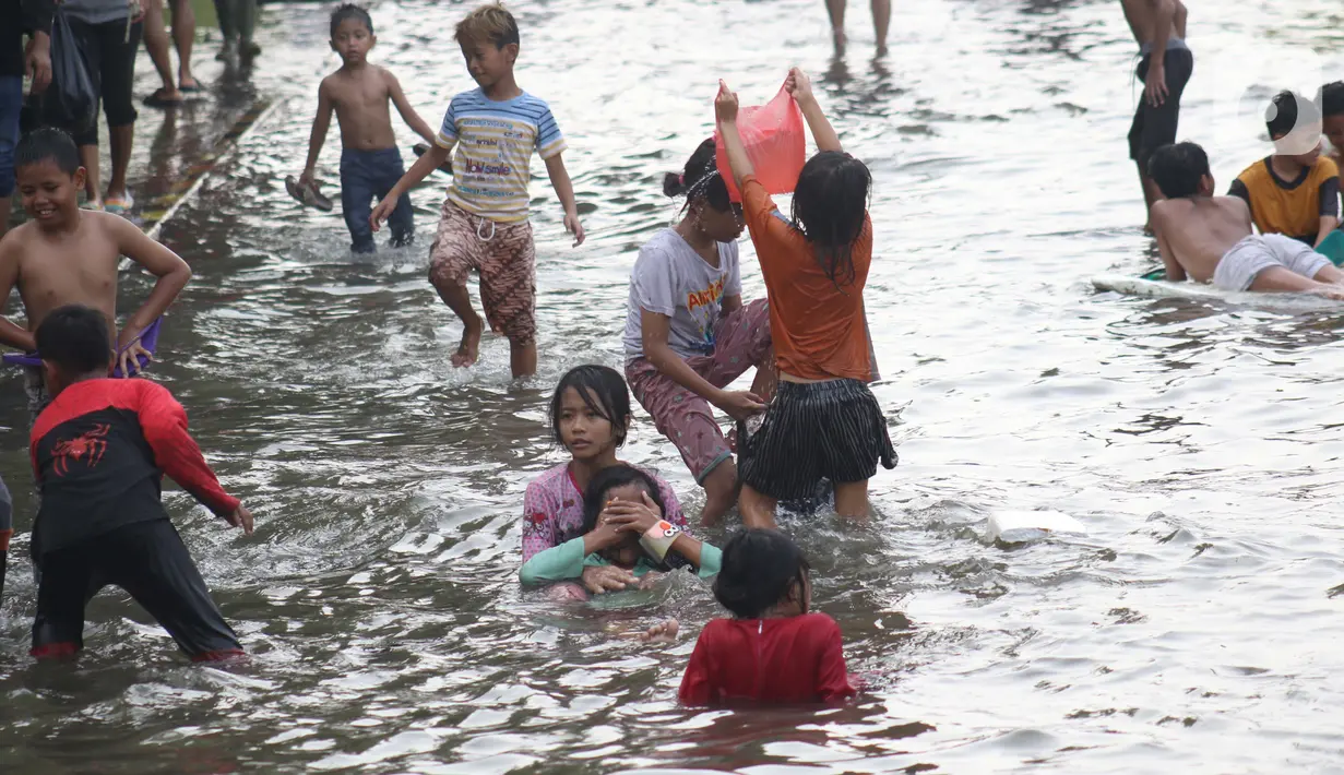 Sejumlah anak-anak bermain di genangan air akibat banjir rob di kawasan pintu masuk Pelabuhan Nizam Zachman, Muara Baru, Jakarta, Jumat (5/6/2020). Banjir rob di Pelabuhan Muara Baru tersebut terjadi akibat cuaca ekstrem serta pasang air laut. (Liputan6.com/Helmi Fithriansyah)