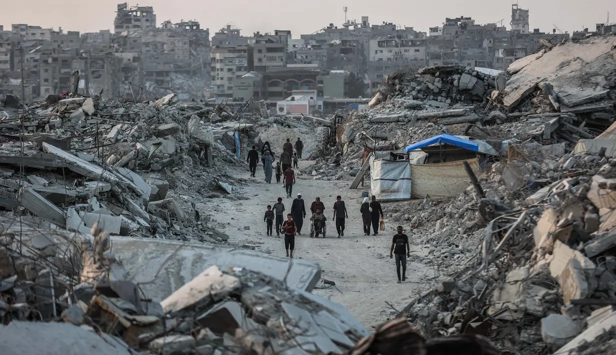 Akses bantuan, terutama ke wilayah utara Gaza, masih sangat terbatas, dan banyak permintaan bantuan ditolak oleh pihak berwenang Israel. Tampak dalam foto, warga Palestina berjalan di antara puing-puing bangunan yang hancur di Jabalia, di bagian utara Jalur Gaza, pada Jumat 7 November 2025. (Omar AL-QATTAA/AFP)