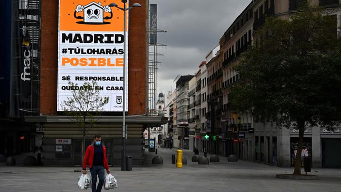 Warga membawa tas belanja berjalan di jalan yang sepi di tengah kebijakan lockdown nasional untuk menekan penyebaran virus corona di Madrid pada 27 Maret 2020.  Spanyol menjadi negara kedua dengan jumlah kematian terbanyak akibat wabah virus corona, di bawah Italia. (Photo by Gabriel BOUYS / AFP)