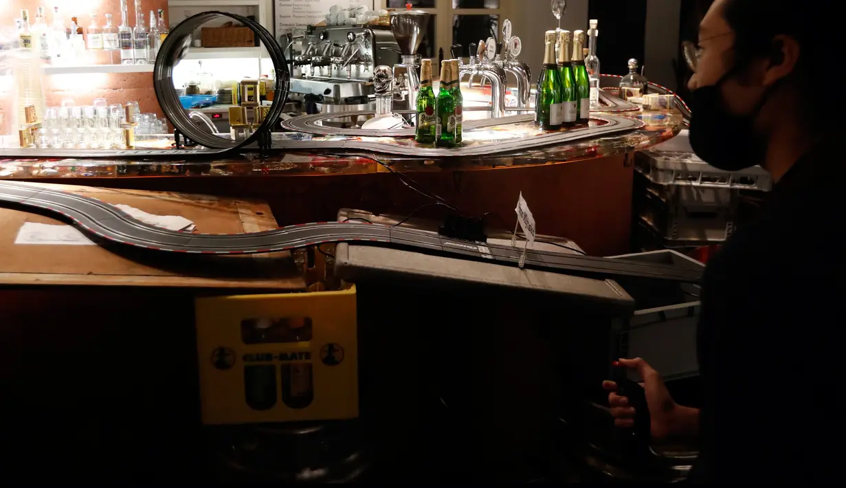 Pekerja menikmati lintasan mobil balap mainan yang dipasang di sebuah bar di Praha, Republik Ceko, 15 Oktober 2020. Lintasan di atas meja bar itu cukup menghibur untuk menghabiskan waktu di tengah larangan buka restoran dan hanya menerima pesanan untuk dibawa pulang saja. (AP Photo/Petr David Josek)