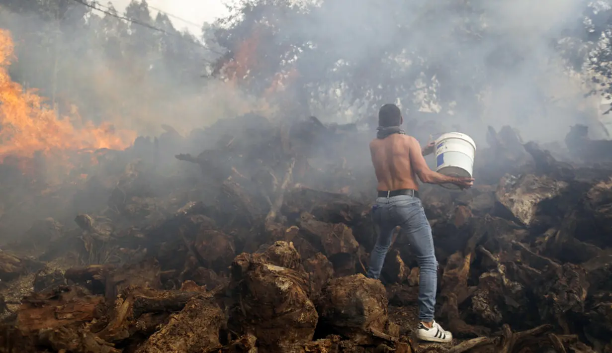 Seorang penduduk setempat menggunakan ember untuk mencoba menghentikan kebakaran hutan yang mencapai rumah-rumah di Desa Figueiras, di luar Leiria, Portugal, 12 Juli 2022. Ratusan petugas pemadam kebakaran di Portugal terus memadamkan api di pusat negara yang memaksa evakuasi puluhan orang dari rumah mereka sebagian besar di desa-desa sekitar Santarem, Leiria, dan Pombal. (AP Photo/Joao Henriques)